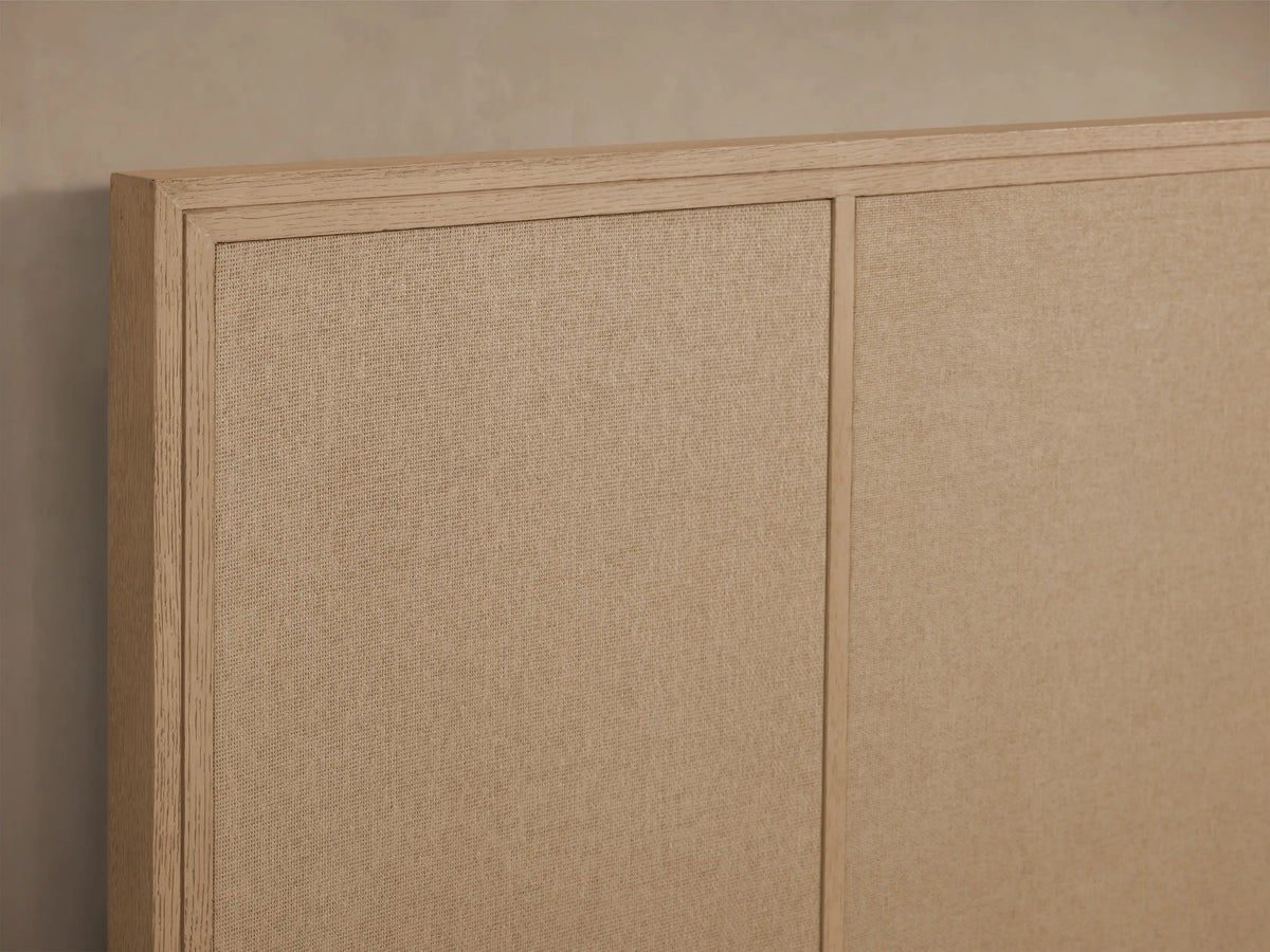 Front view of the Olina Bed with a natural oak wood frame and textural tan raffia panels. White quilted bedding.