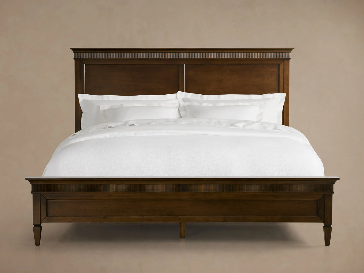 Ottavia Bed with Tanganika wood frame, rich dark finish, white bedding, headboard and footboard in view, neutral background.