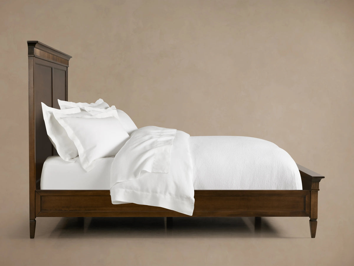 Ottavia Bed made of Tanganika wood with a dark brown finish, featuring a high headboard and white bedding on a wooden floor.