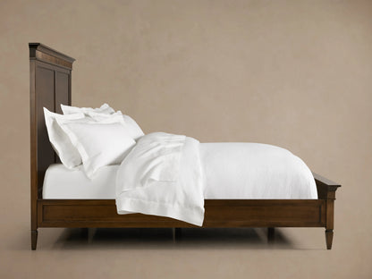Ottavia Bed made of Tanganika wood with a dark brown finish, featuring a high headboard and white bedding on a wooden floor.