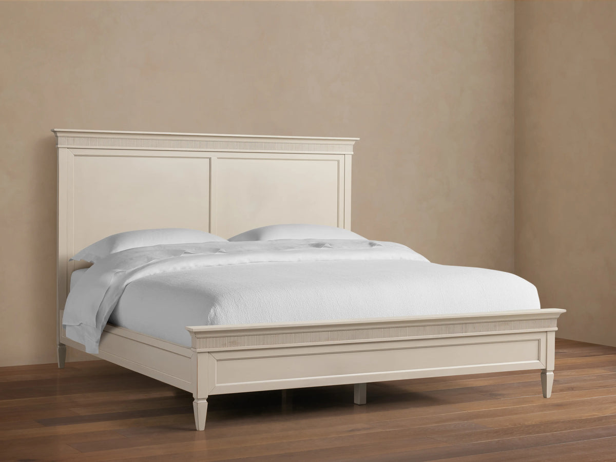 Ottavia Bed in light wood finish with elegant paneled headboard, fitted with white bedding, sitting on wooden floor.