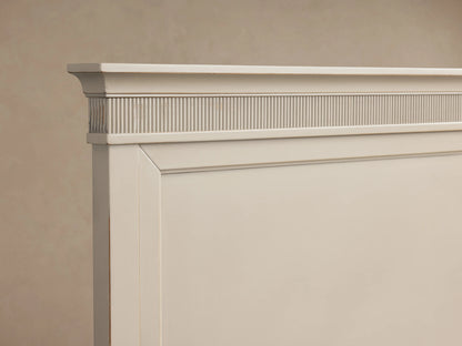Ottavia Bed in light wood finish with elegant paneled headboard, fitted with white bedding, sitting on wooden floor.