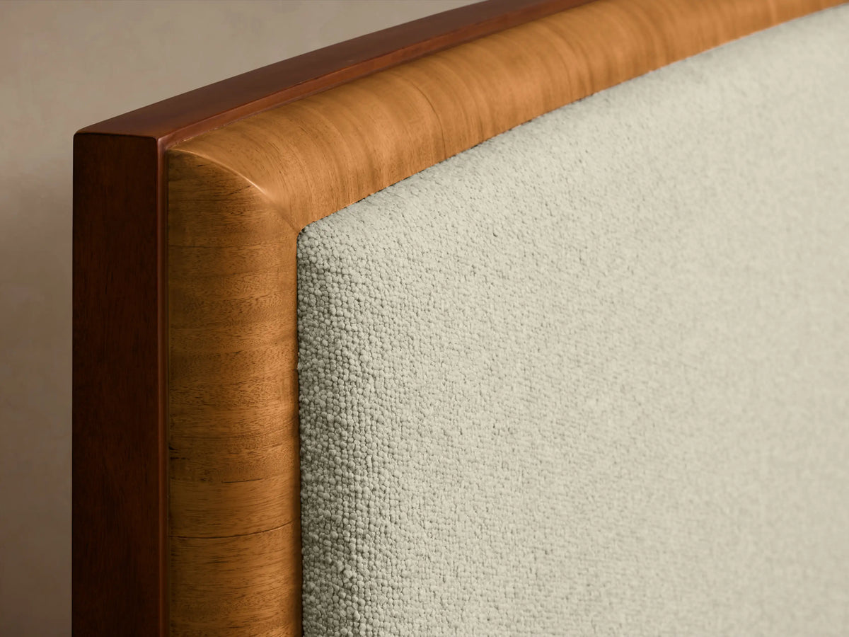 Front view of the Palma Bed with a cream upholstered headboard, cerajeira wood veneer frame, and mahogany plinth base.