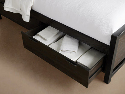 Dark wood Palmer Storage Bed with an open drawer, showing neatly folded white linens inside. Part of the bed frame and bedding are visible.