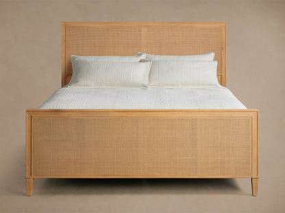 Front view of the natural wood Pearson Cane Bed, featuring a woven cane headboard and footboard, dressed with white bedding.