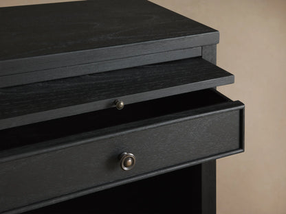 Dark wood Pearson Nightstand with one drawer, pull-out tray, and open shelf, on a wood floor against a beige wall.