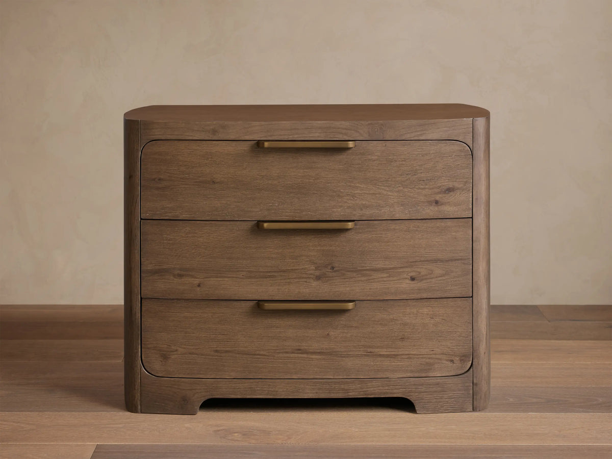 Front view of the brown Redding Nightstand, featuring three drawers with brass bar pulls, and rounded top and bottom edges.