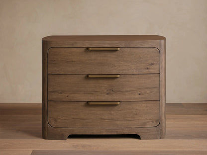 Front view of the brown Redding Nightstand, featuring three drawers with brass bar pulls, and rounded top and bottom edges.
