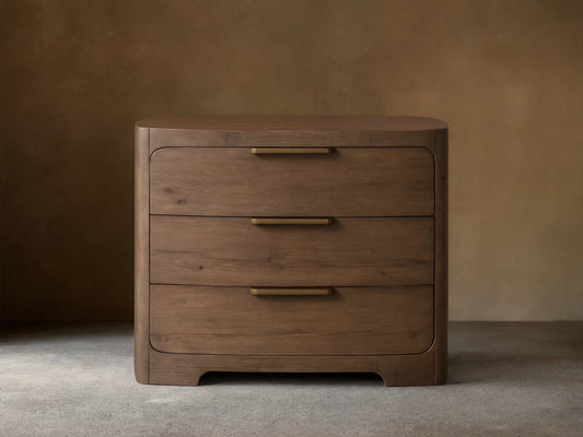 Front view of the brown Redding Nightstand, featuring three drawers with brass bar pulls, and rounded top and bottom edges.