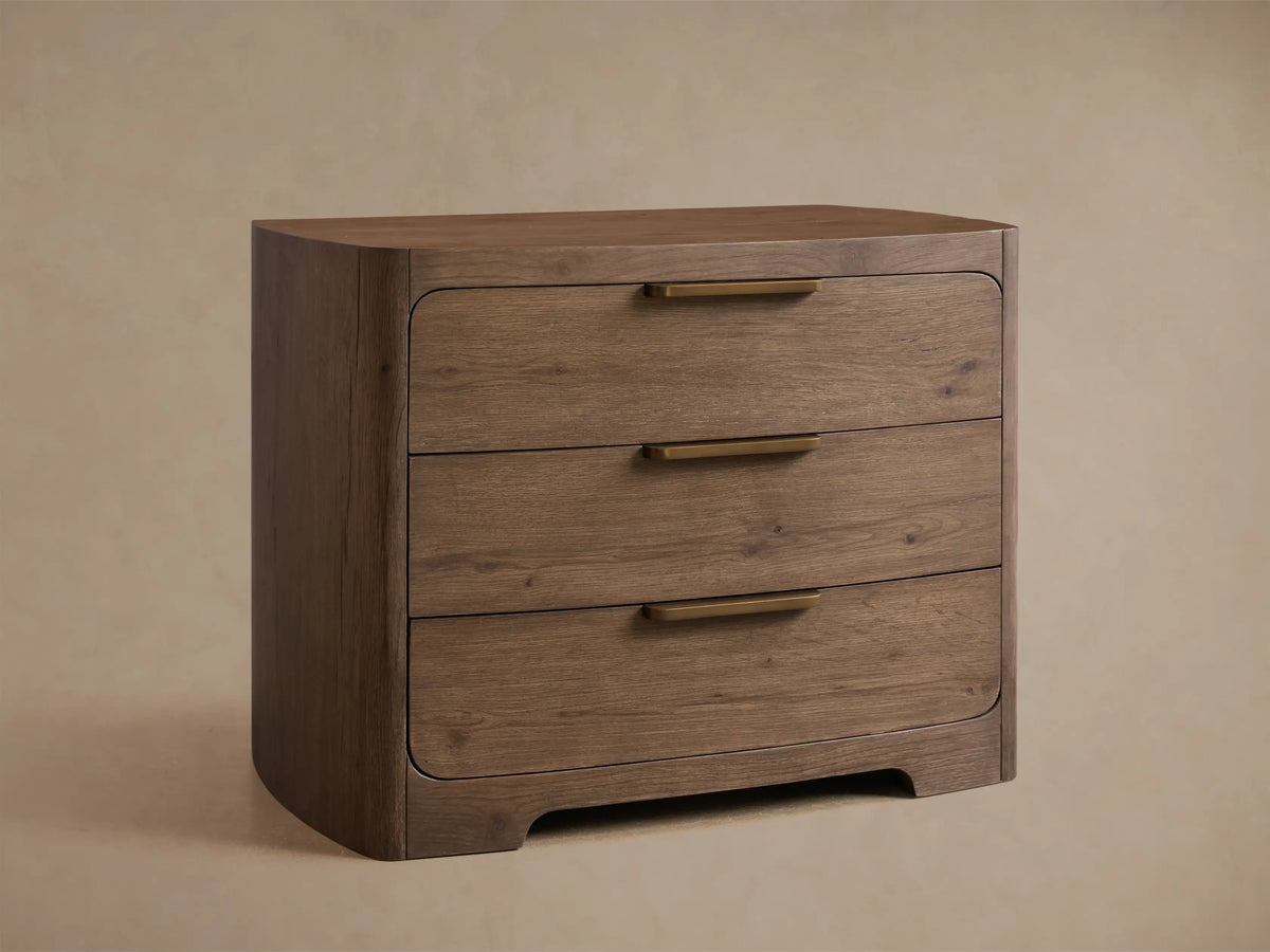 Front view of the Redding Nightstand, a medium brown wooden nightstand with rounded edges, three drawers, and brass pulls.