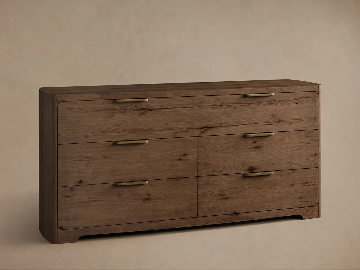 Angled front view of the Redding Six-Drawer Dresser, a medium brown wooden dresser with grain, six drawers, brass bar handles, and rounded edges.