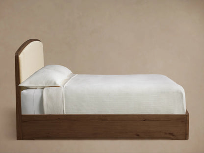 Side profile of the Redding Bed with a dark wood frame and arched cream upholstered headboard, dressed in white bedding.
