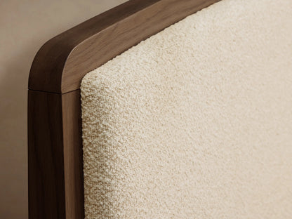 Close-up of the Redding Bed, showing a dark brown wooden frame with rounded edges and a light beige textured upholstered panel.