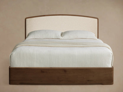 Angled view of the Redding Bed with a dark brown wood frame, cream upholstered headboard, and white vertically ribbed bedding.