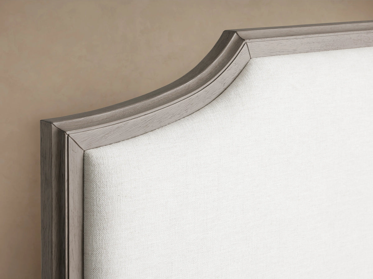 St. Martin Bed in oak wood, features a high upholstered headboard, white bedding, and a simple frame design on a beige background.