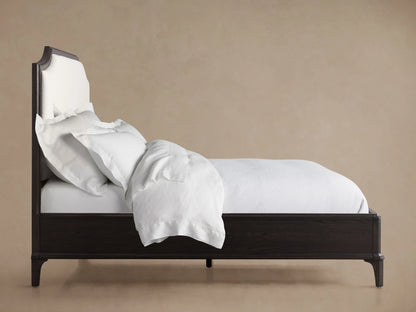 St. Martin Bed headboard with dark oak wood frame and light fabric upholstery, featuring a curved top design against a neutral wall.