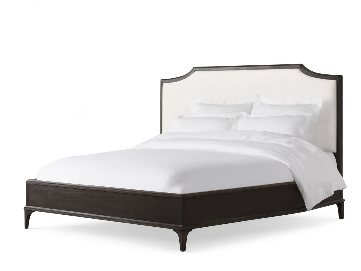 St. Martin Bed with dark oak frame, white upholstered headboard, white bedding, on hardwood floor against beige wall.