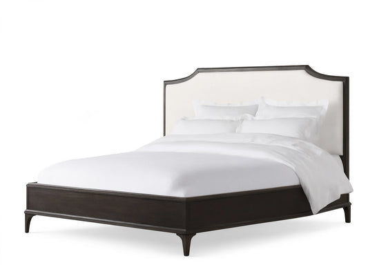 St. Martin Bed with dark oak frame, white upholstered headboard, white bedding, on hardwood floor against beige wall.