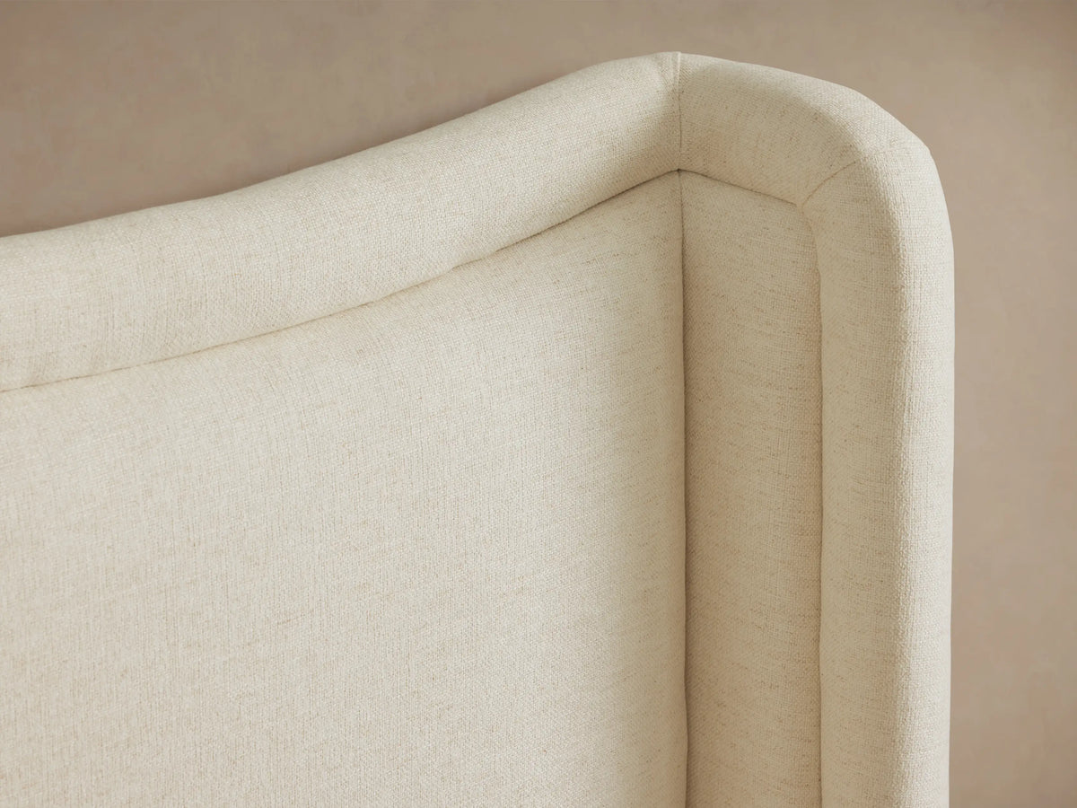 Winslet Bed, a cream upholstered bed with a gently curved, wingback headboard, white ribbed bedding, and a gray throw.