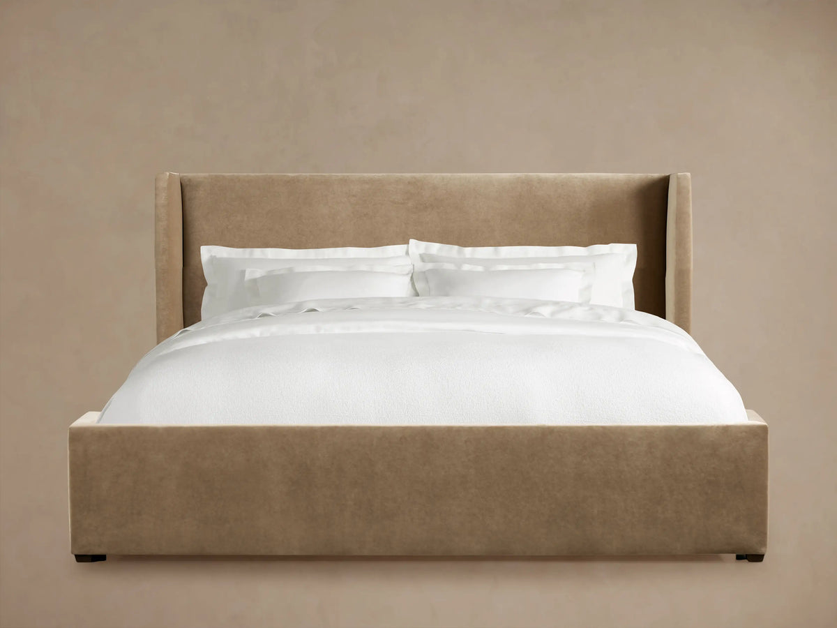 Wyller Bed with a tall, winged, beige upholstered headboard and frame. Dressed with crisp white pillows and duvet.