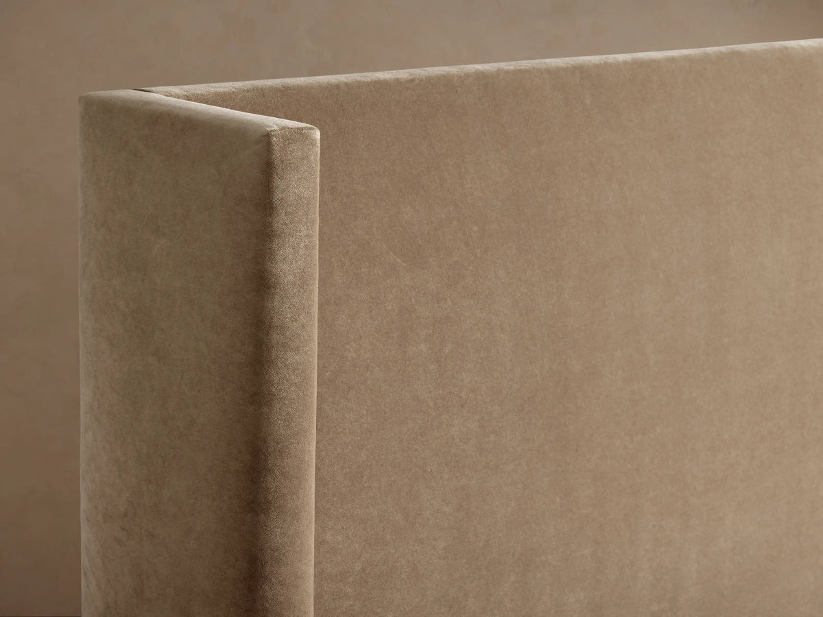 Wyller Bed: Close-up of a plush, light brown upholstered headboard corner, highlighting the soft fabric texture.