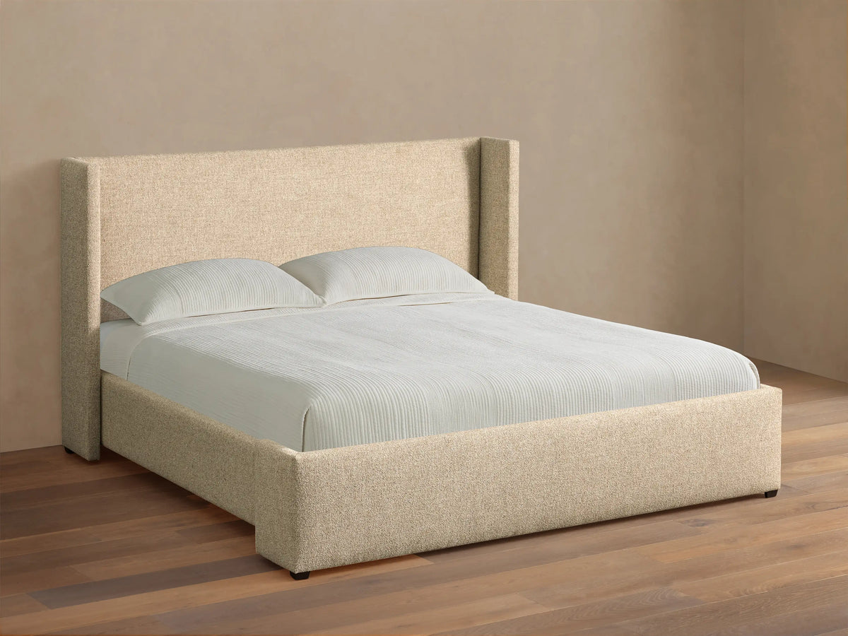Front view of the beige upholstered Wyller Bed featuring an angled wingback headboard, made with white bedding.