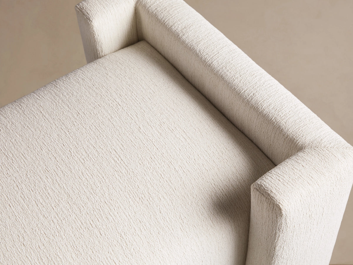 Close-up of Wyller Bench in textured Tania Cashmere off-white fabric, showing seat and armrest from a high angle.