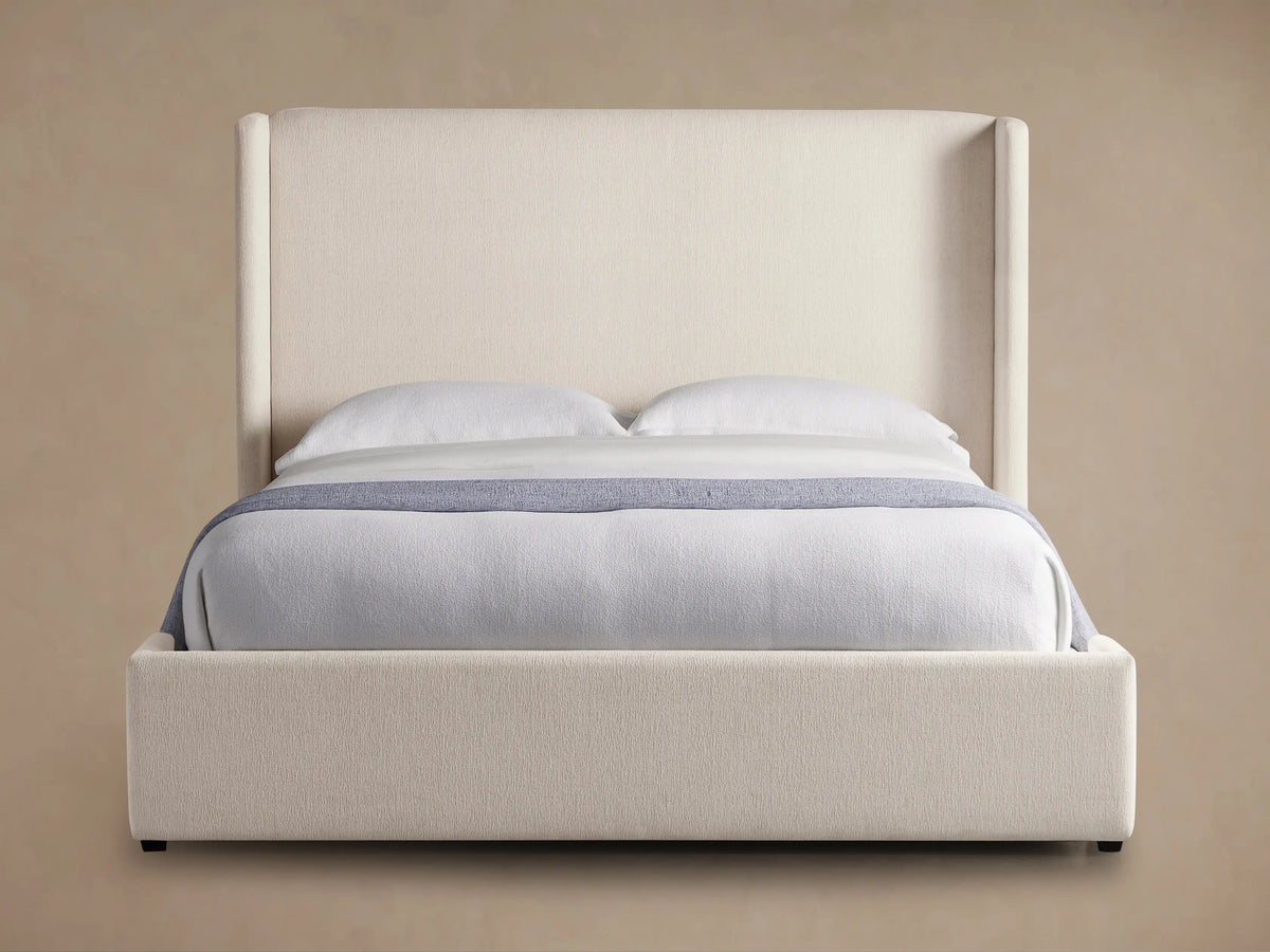 Wyller Bed with tall, cream upholstered headboard & frame, white bedding & light blue throw on wood floor.