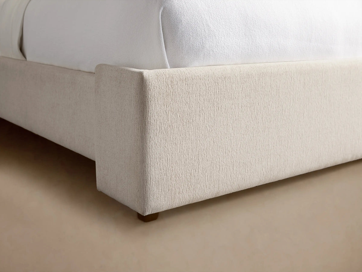 Wyller Bed with tall, light beige upholstered headboard, white bedding, and a light blue throw blanket.