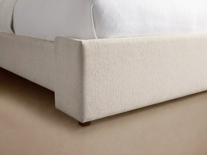 Wyller Bed with tall, light beige upholstered headboard, white bedding, and a light blue throw blanket.