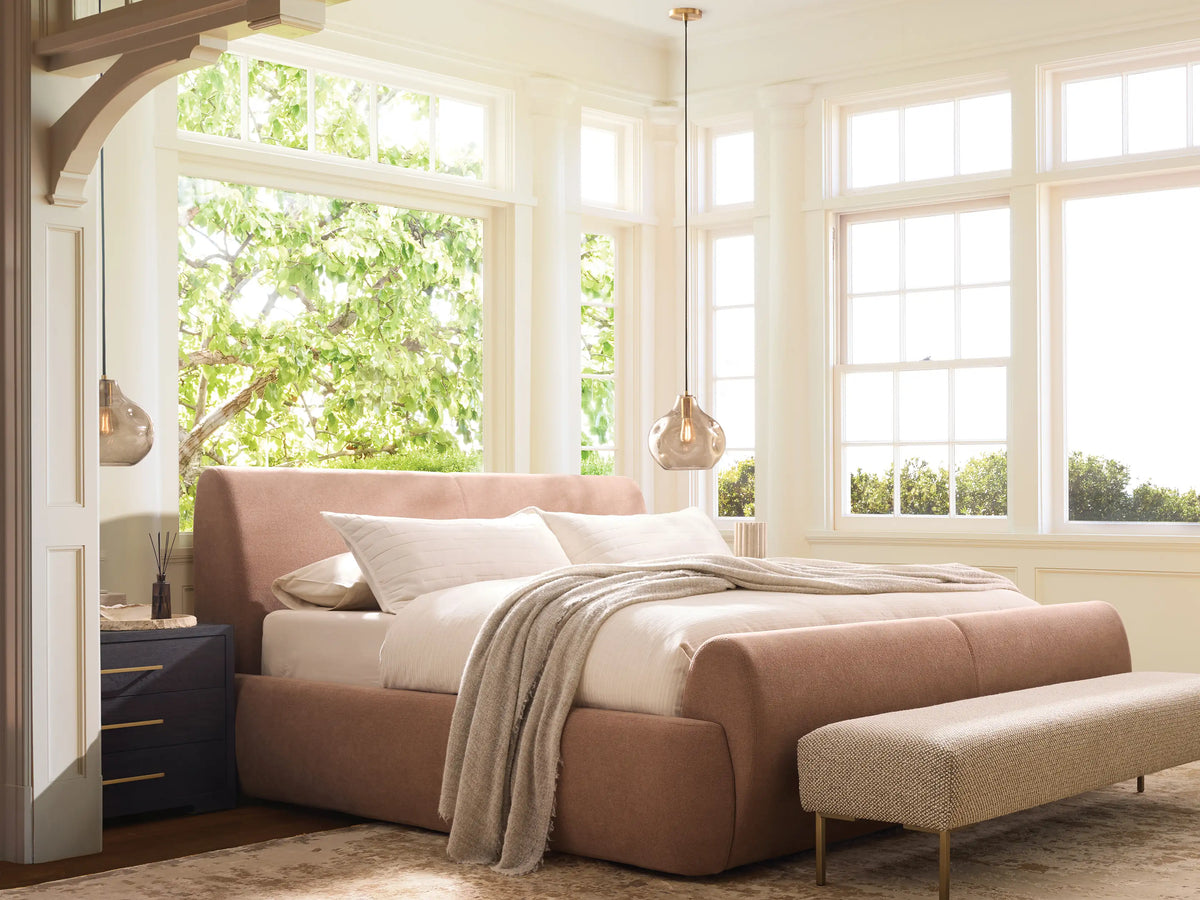 Wynn Bed: Light pink upholstered bed with rounded headboard, footboard & sides; white pillows & textured blanket; on wood floor.