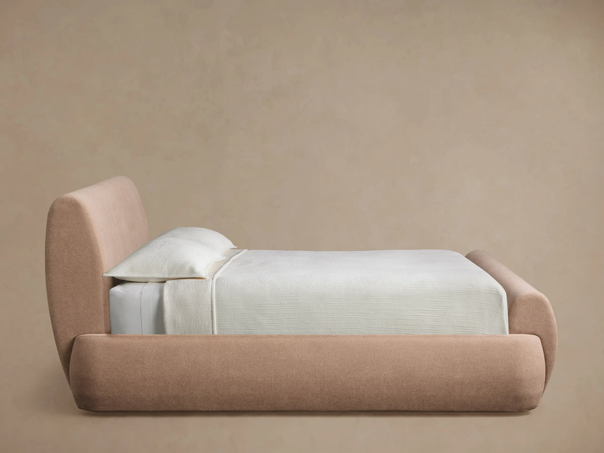 Close-up of the Wynn Bed's rounded headboard in light brown textured upholstery fabric with two parallel stitched seams.