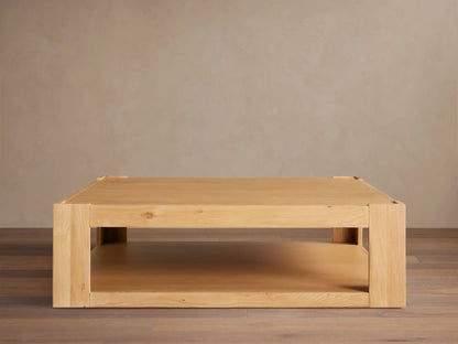 Devon Coffee Table, square natural oak wood. Features a thick top, sturdy square legs, and a practical lower storage shelf.