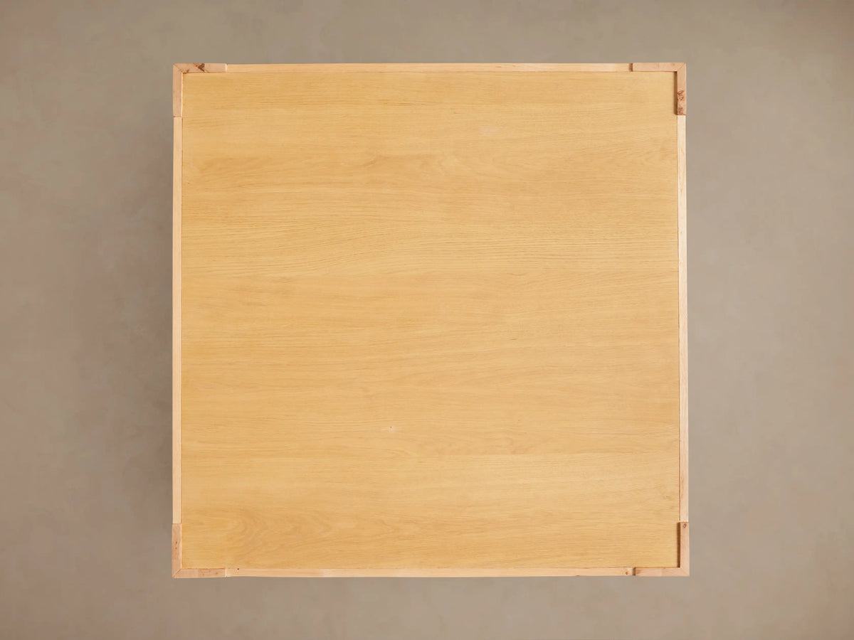 Close-up of natural oak Devon Coffee Table with visible wood grain, thick leg, and lower shelf. Warm light brown wood.