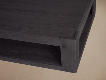 Black oak Devon Coffee Table, rectangular with a lower shelf, angled on wood floor against a beige wall.