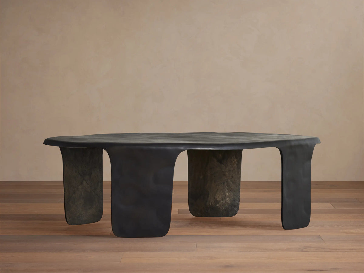 Melbourne Coffee Table, dark bronze metal, featuring an organic, wavy top and thick, sculpted legs on a wooden floor.