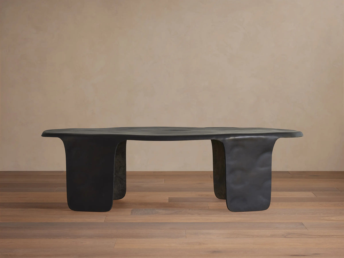 Melbourne Coffee Table, dark bronze metal, featuring an organic, wavy top and thick, sculpted legs on a wooden floor.