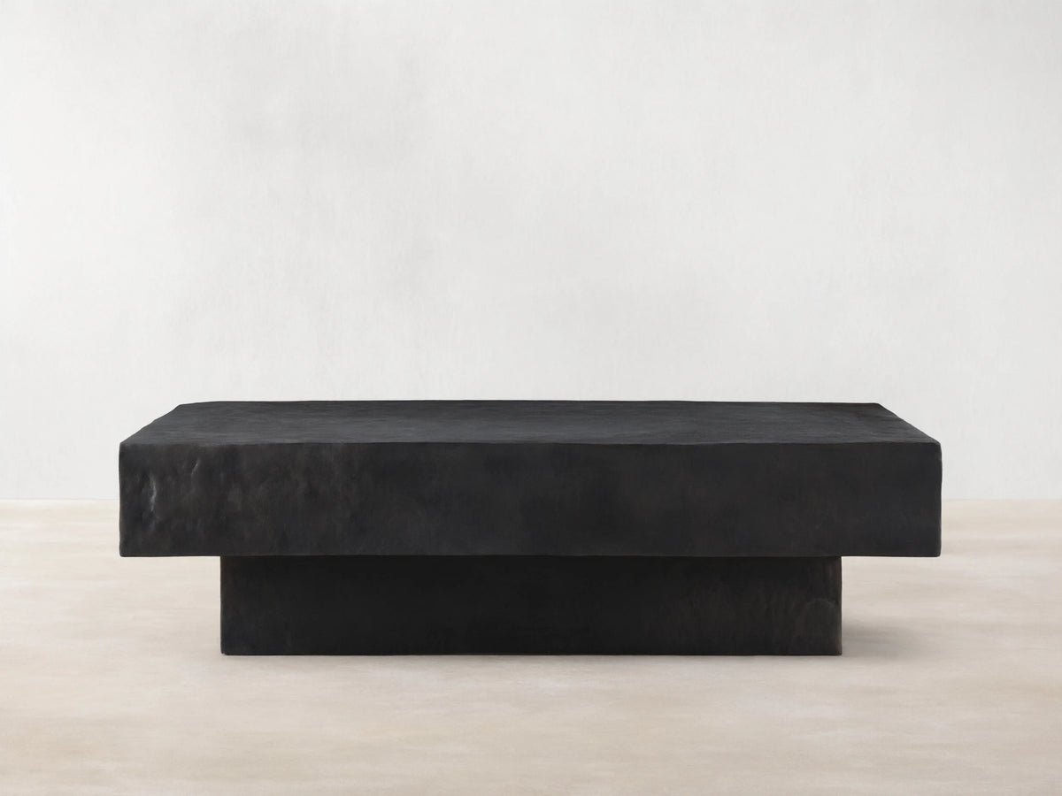 Sydney Coffee Table in a minimalist design, featuring a rectangular shape with a dark, textured finish, set on a hardwood floor.
