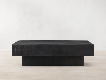 Sydney Coffee Table in a minimalist design, featuring a rectangular shape with a dark, textured finish, set on a hardwood floor.