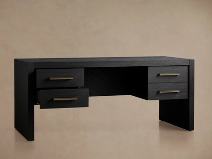 Black Bodhi Executive Desk with visible wood grain, four drawers with brass pulls, centered on a wood floor against a neutral wall.