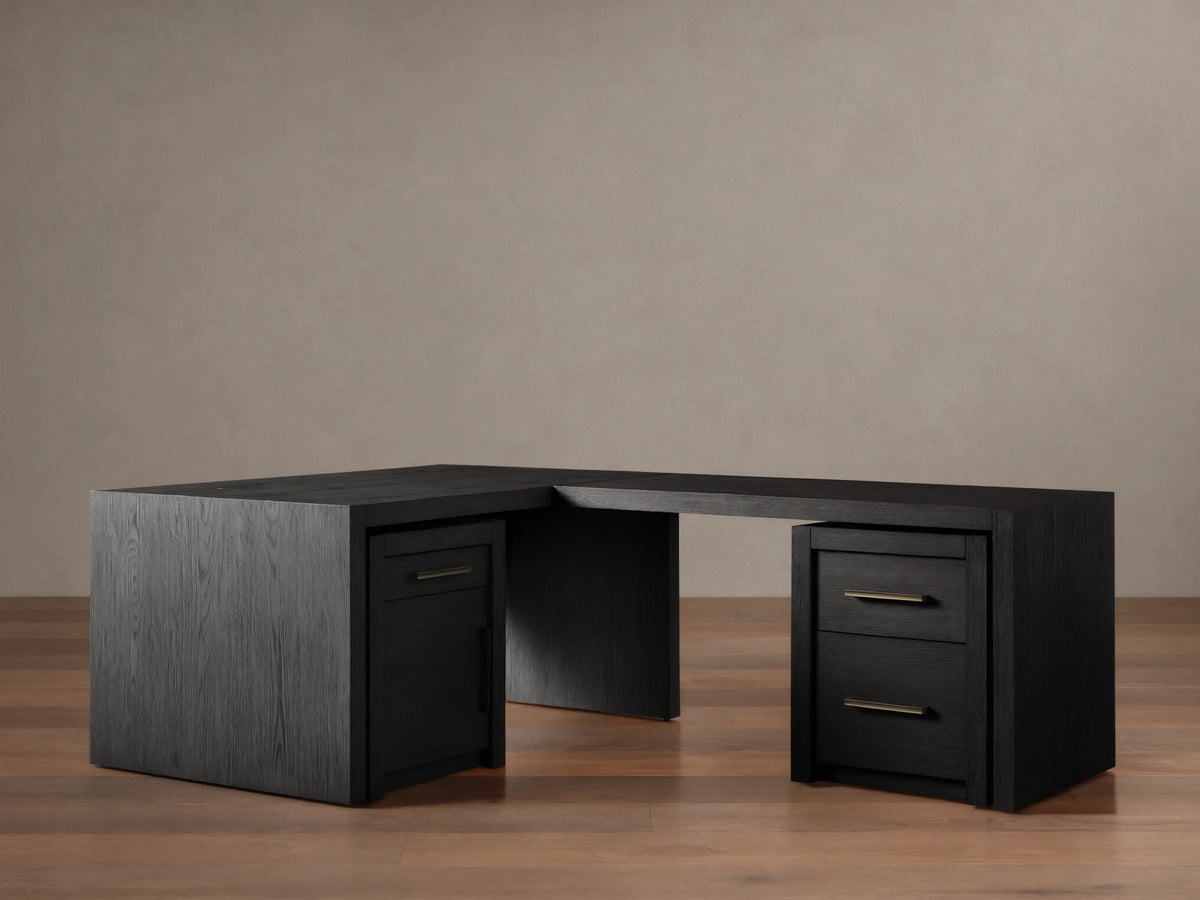 Bodhi Modular Desk, L-shaped, dark wire-brushed oak, 3 drawers with brass pulls, on wooden floor against a tan wall.