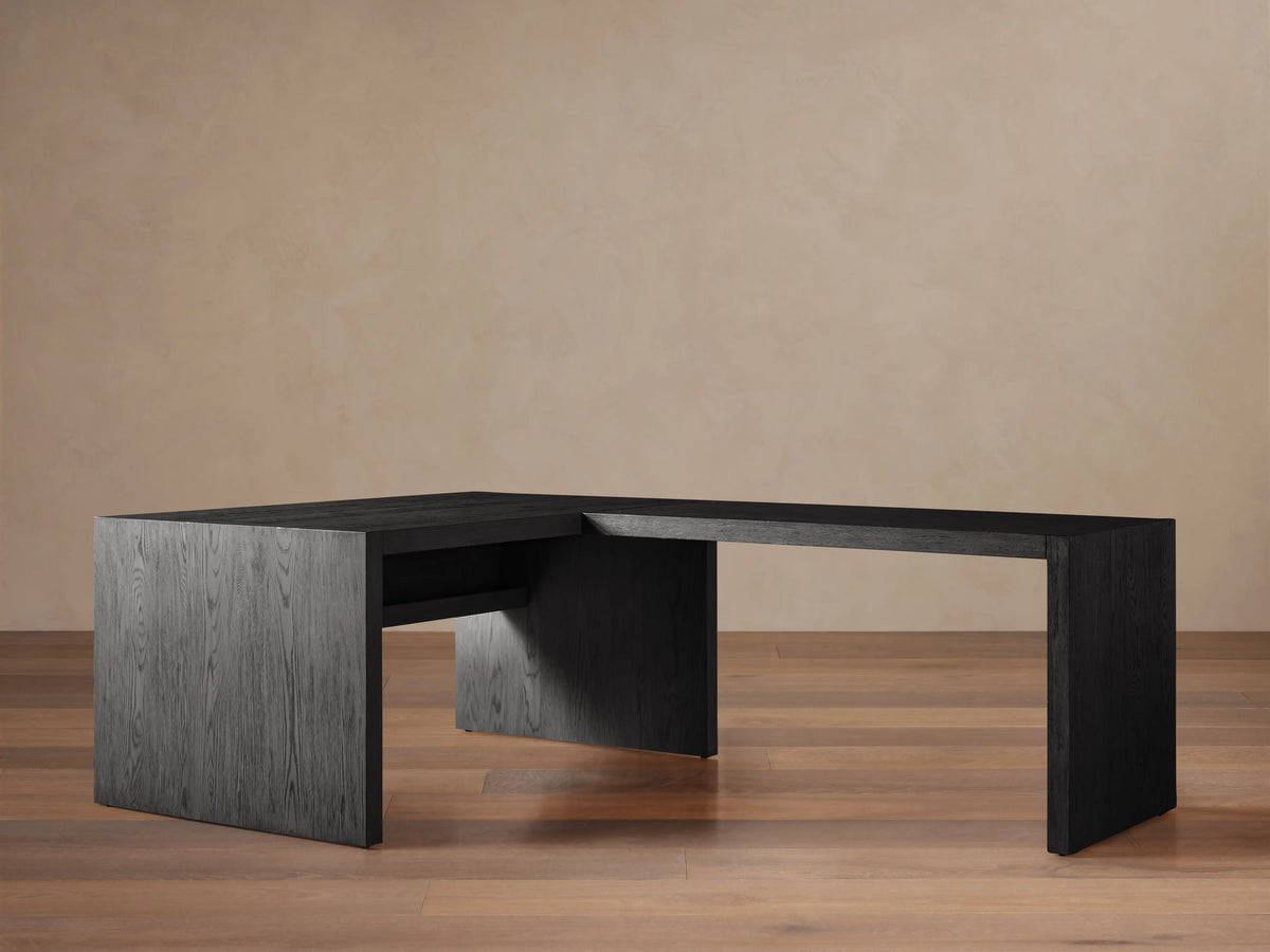 Bodhi Modular Desk, L-shaped, dark wire-brushed oak, 3 drawers with brass pulls, on wooden floor against a tan wall.