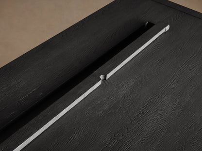 L-shaped Bodhi Modular Desk with Return Desk in dark charcoal gray wood, visible grain, on a wood floor against a plain wall.