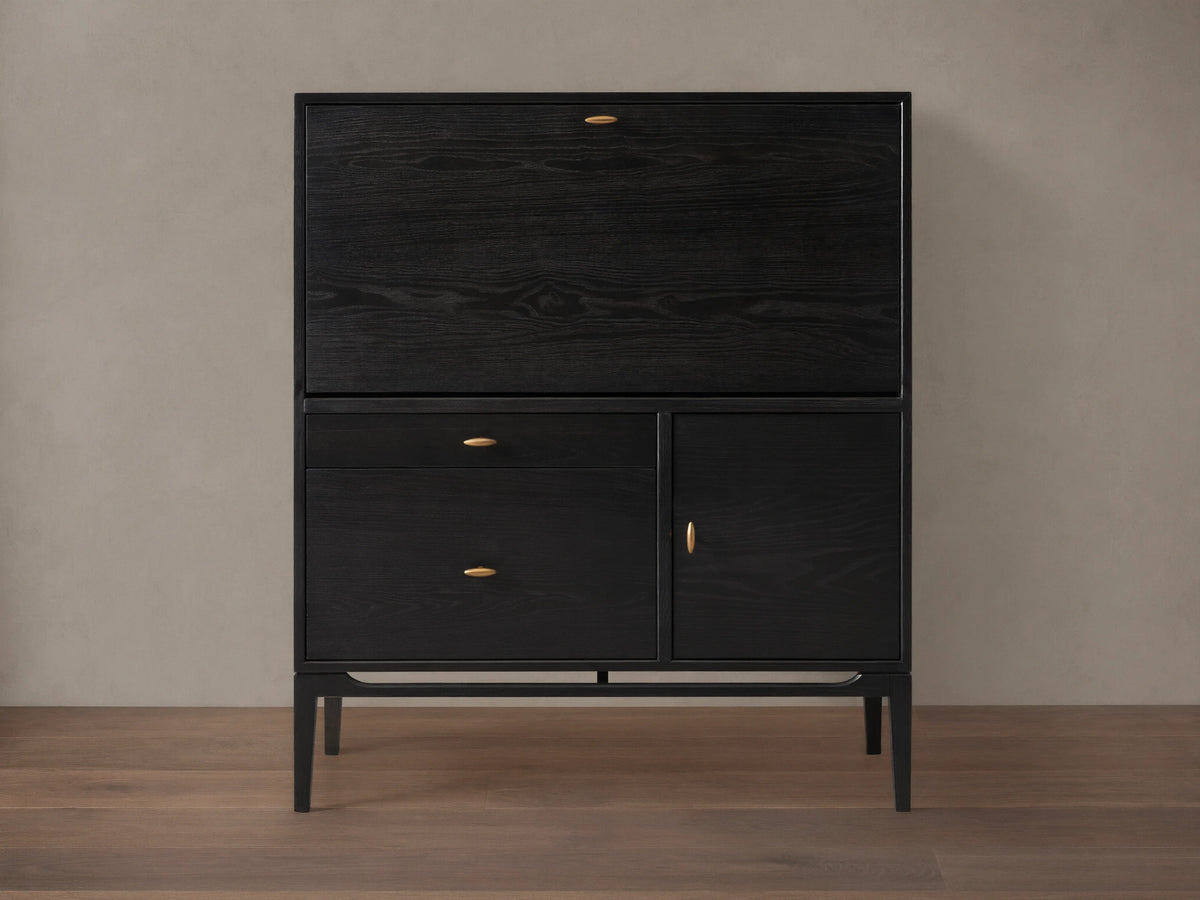 Dark ash wood Brock Hideaway Desk with a fold-down front, two drawers, and a side cabinet, featuring gold handles.