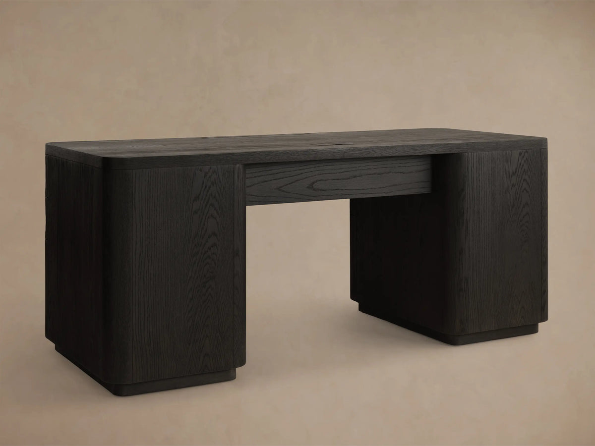 Detail of a dark charcoal wooden desk from above, with two open drawers featuring rounded fronts and vertical bronze handles.