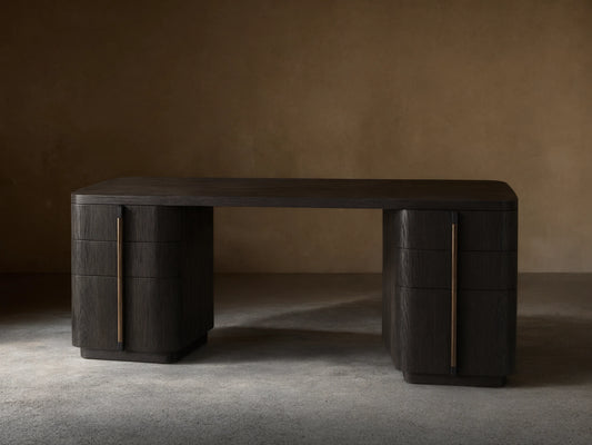 Front view of a dark wood finish writing desk with rounded corners and six drawers featuring long, vertical bronze-toned pulls.