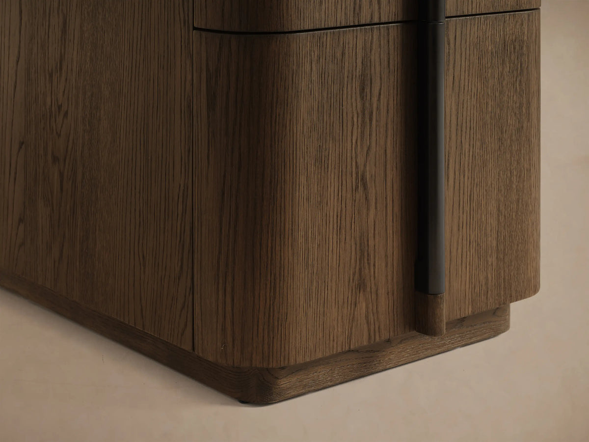 Close-up of a rich brown wood cabinet with an open drawer, curved front, and black vertical handle.