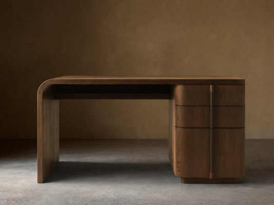 Front view of a dark brown wooden desk with three curved drawers on the left and a continuous tabletop and right leg.