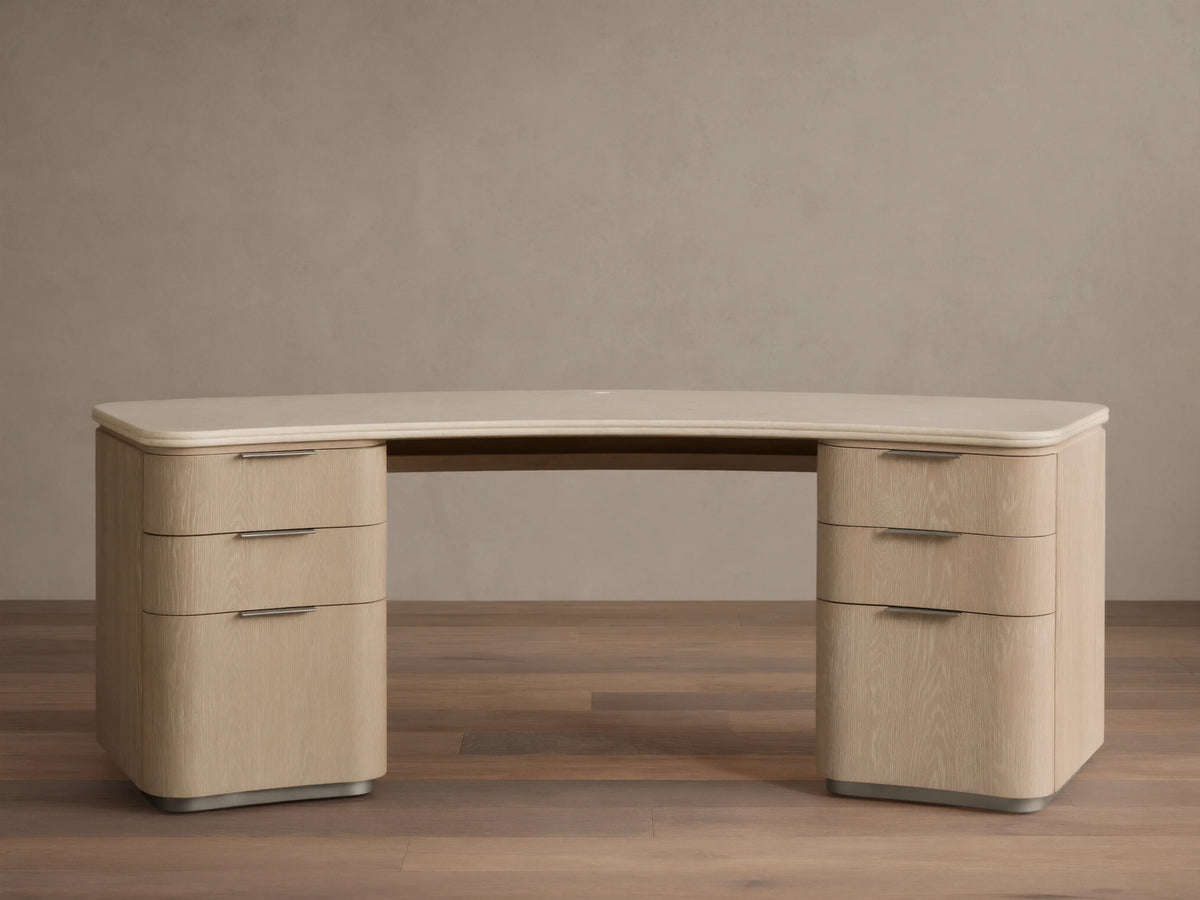 Caden Executive Desk. Light sand wood with rounded edges, cream marble top, and six drawers with brushed nickel hardware.