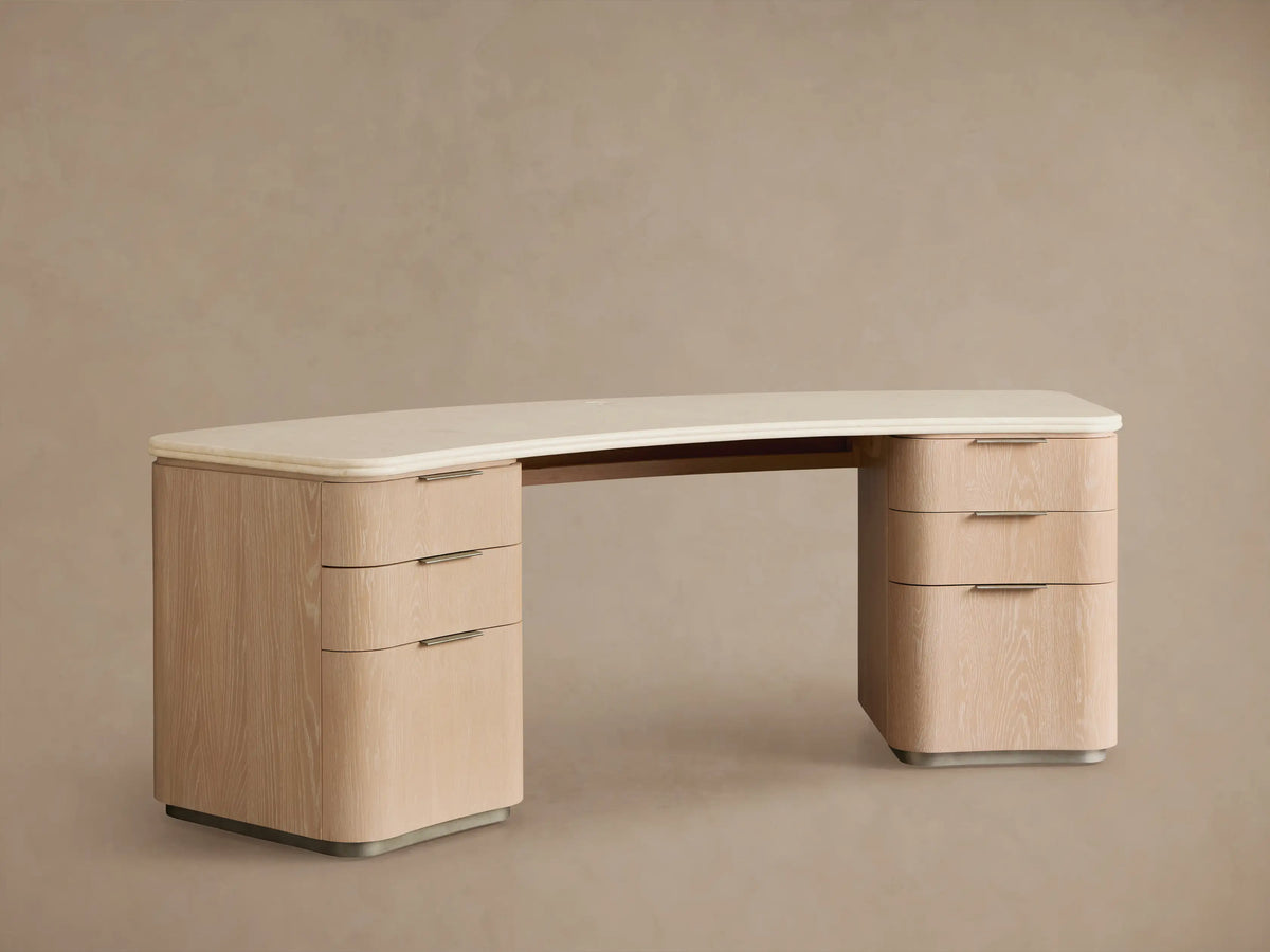 Caden Executive Desk. Light sand wood with rounded edges, cream marble top, and six drawers with brushed nickel hardware.